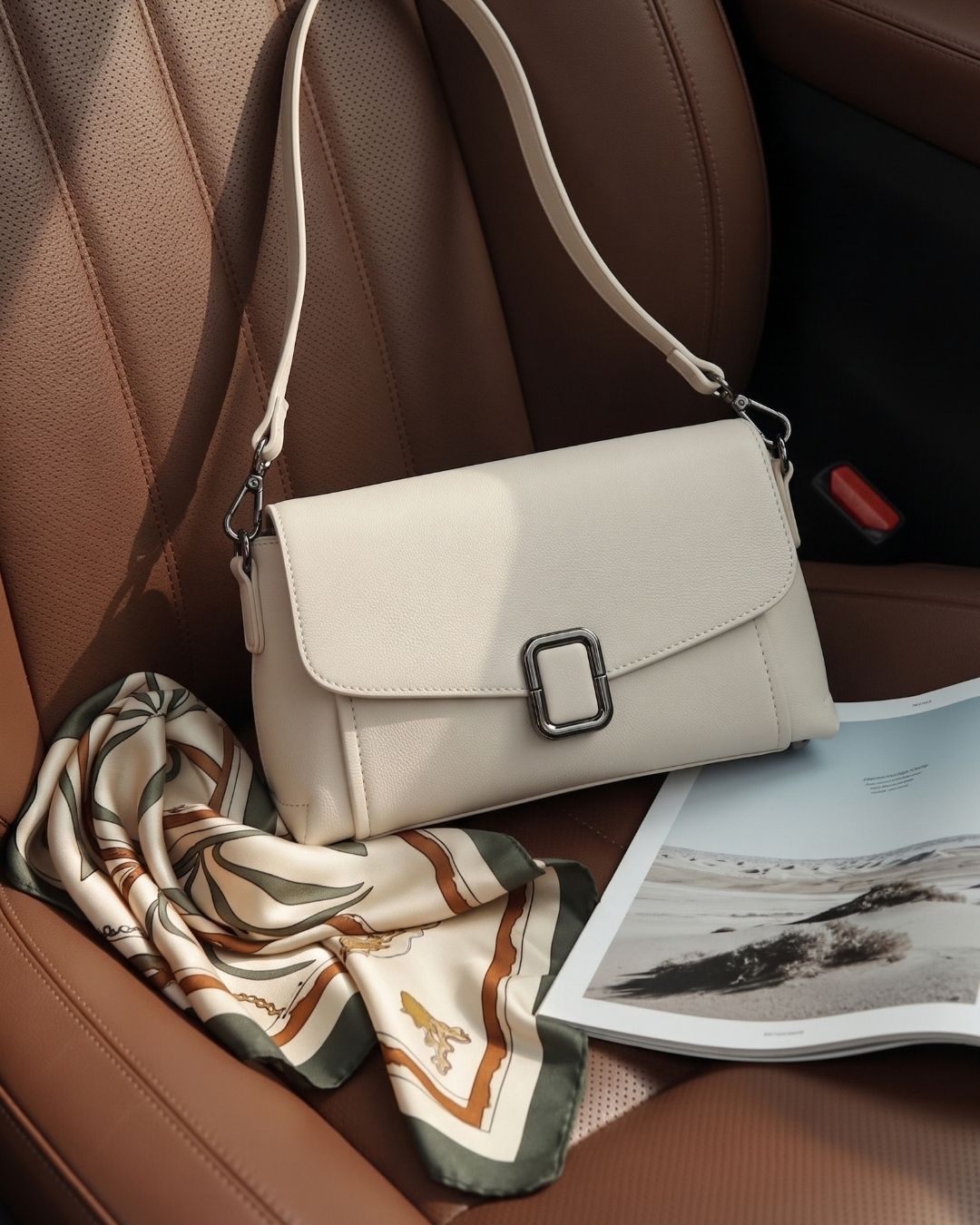 Cream leather crossbody bag with a silk scarf on a tan leather car seat