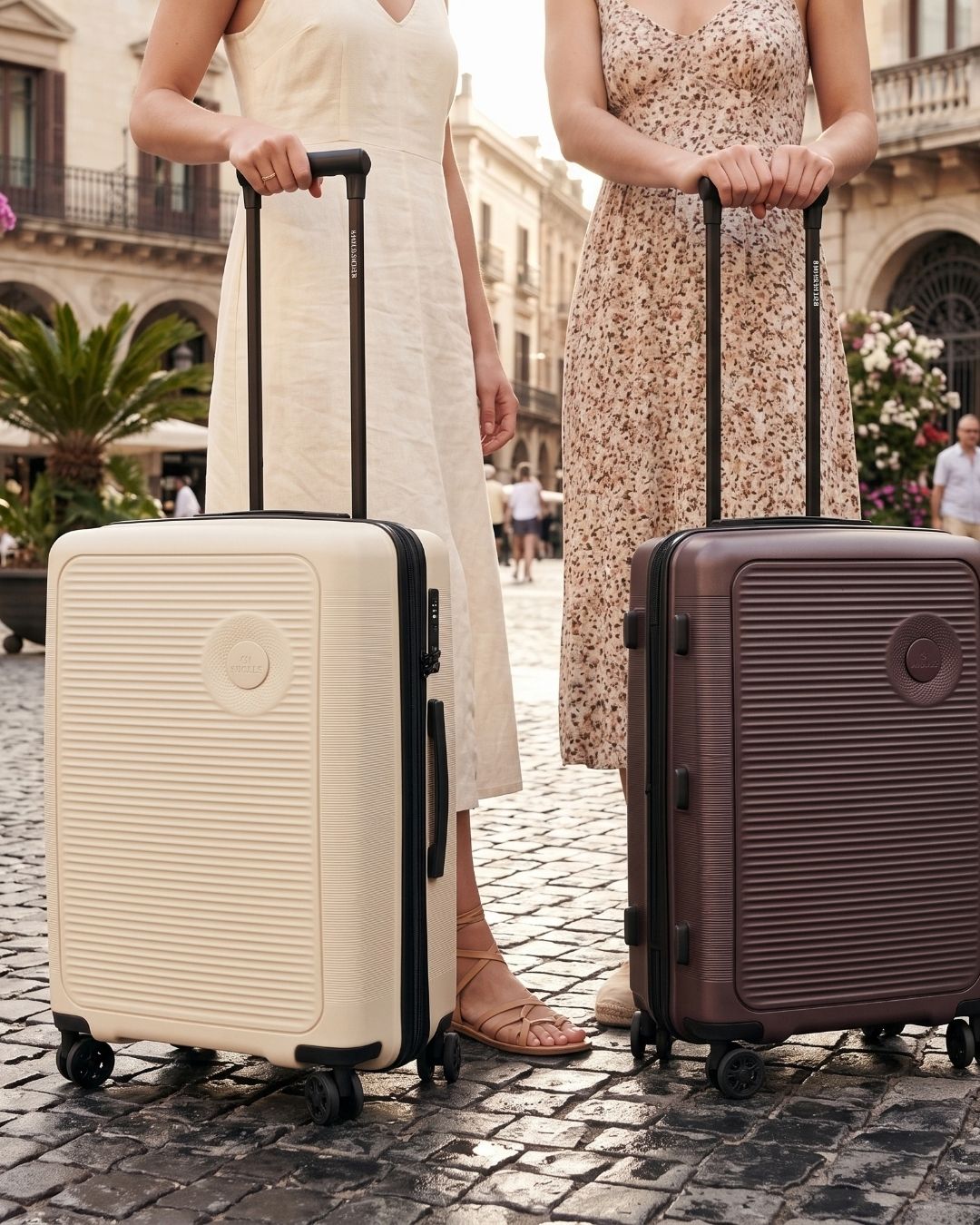 Cream and plum hard shell suitcases beside two women on a cobbled street